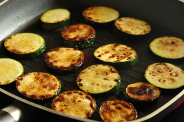 Sliced courgette zucchini cooking in a griddle frying pan on a hob stove
