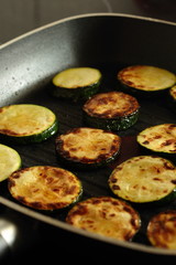 Sliced courgette zucchini cooking in a griddle frying pan on a hob stove