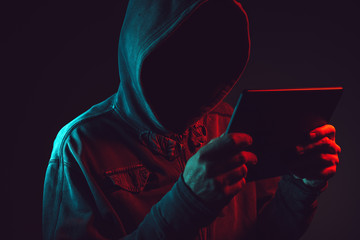 Hooded computer hacker with tablet computer