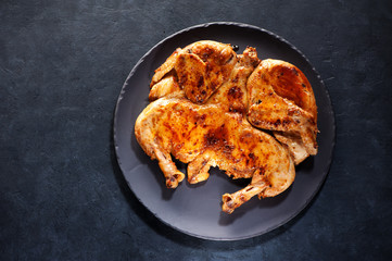 Grilled fried roast Chicken Tabaka on a plate, on a black concrete background, top view