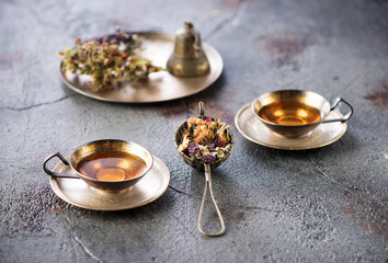 Herbal tea in metal cups and dried herbs on a gray concrete background