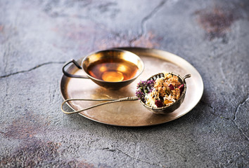 Herbal tea in a metal cup, a vintage strainer on a metal tray on a gray concrete background