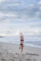 Fototapeta na wymiar attractive young woman practicing yoga in tree pose (Vrksasana) on seashore