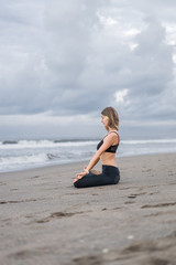 Fototapeta na wymiar side view of beautiful young woman practicing yoga in lotus pose and meditating on seashore
