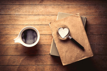 White cup with coffee and books with magnifier, heart on wooden table. High angle view