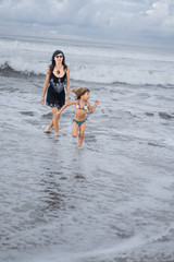 mother and daughter walking by seashore together on cloudy day
