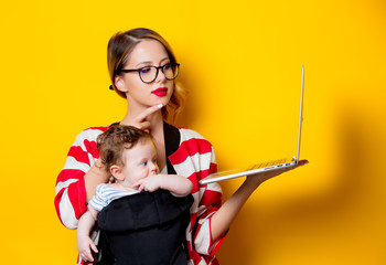 little baby in carrier and mother with laptop computer on yellow background