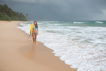 Female surfer walking along the ocean with a board in hands.