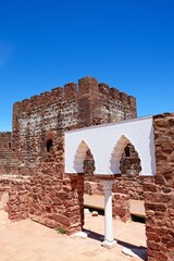 View of the Medieval ruins inside the castle showing the vaulted Moorish windows of the palace of balconies with the battlements and one of the towers to the rear, Silves, Portugal.