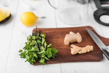 Ingredients for making ginger tea on the recipe: ginger, lemon, mint, water and honey on white wooden background.