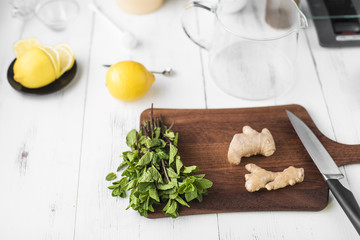 Ingredients for making ginger tea on the recipe: ginger, lemon, mint, water and honey on white wooden background.