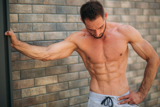 Young athlete posing with a torso for photography on a brick wall background. Bodybuilder, athlete with pumped muscles, breast and arm rescue