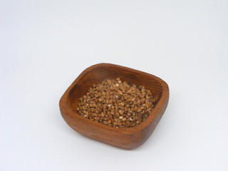 Dry buckwheat groats in wooden plate isolated