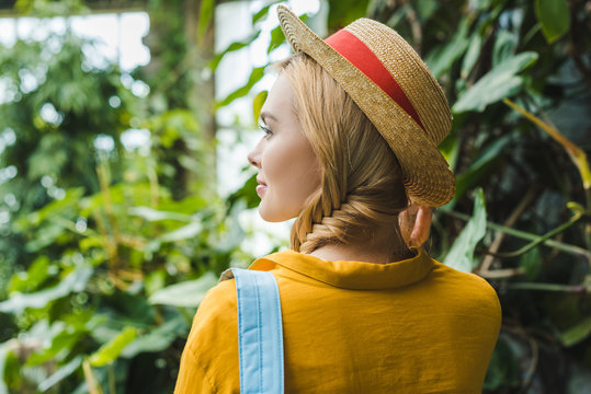 rear view of beautiful young woman in straw hat surrounded with tropical plants