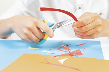 Child hands cutting colored paper with scissors at the table