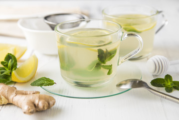 Ginger tea with mint, lemon and honey in a glass cup on a white wooden table