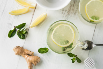 Ginger tea with mint, lemon and honey in a glass cup on a white wooden table, top view