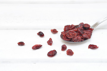 Dried cranberries in a spoon on white wooden background