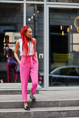 Fashionable african american girl at pink pants and red dreads posed outdoor.