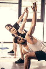handsome sportsmen simultaneously exercising and stretching in gym