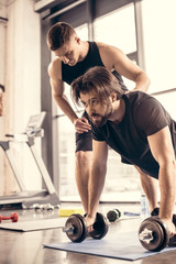 Fototapeta na wymiar handsome sportsman doing push ups on dumbbells in gym