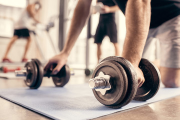 Fototapeta na wymiar cropped image of sportsman preparing doing push ups on dumbbells in gym