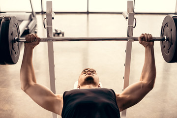 Naklejka premium Handsome muscular sportsman lifting barbell in gym