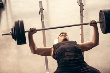 Handsome sportsman lifting barbell on bench press in gym