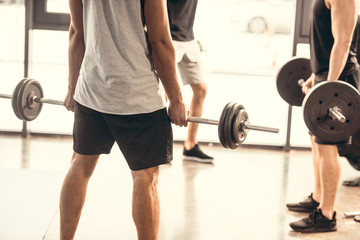 Fototapeta na wymiar cropped shot of sporty young men in sportswear lifting barbells in gym