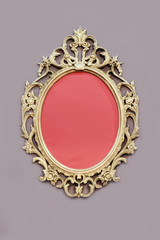 Openwork oval golden colored frame on wall at grey background.