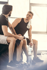 two young sportsmen sitting on tire and looking at each other after workout in gym