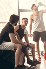 young sportsmen sitting on tire and talking after workout in gym