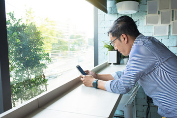 Young Asian businessman dressed in casual style and ware eyeglasses using smart phone in during coffee time in cafe, casual freelance lifestyle or digital nomad concepts