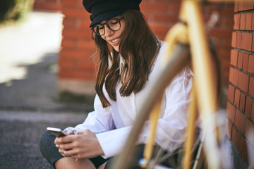 Woman sitting on sidewalk and using smart phone. Next to her yellow bicycle.