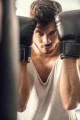 selective focus of handsome young sportsman in boxing gloves looking at camera