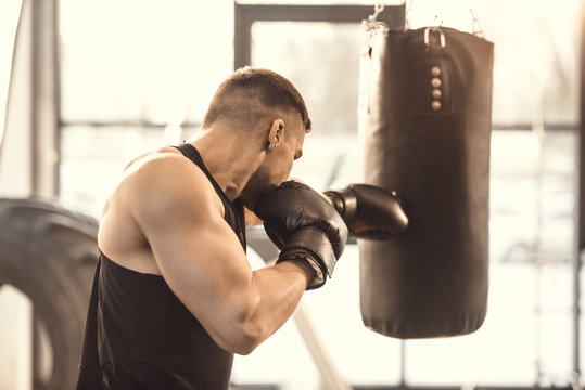 side view of muscular young boxer training with punching bag