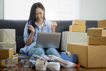 Asian woman smiling with laptop and credit card and boxes at home. freelance and online shopping concept.