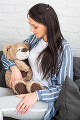 smiling woman with teddy bear resting on sofa at home
