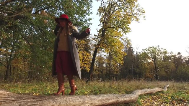fashionable woman walking on a log in an autumn park