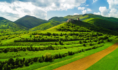 Fototapeta premium Aerial view of Coltesti Fortress in Transylvania, Romania on a sunny spring day with green hills around and beautiful blue sky with clouds