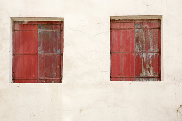 Zwei Fenster mit roten verfallenen und abgeblätterten Fensterläden eingebettet in eine weiss gekalkte Wand. Ein roter Traum.