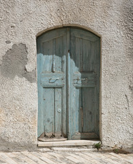 In einer abbröckelnden Mauer eingefasste Doppeltür aus grüngrauem Holz führt zum Garten