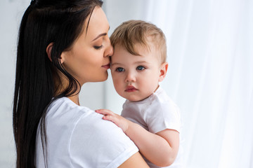 smiling tender mother holding cute baby boy in hands at home