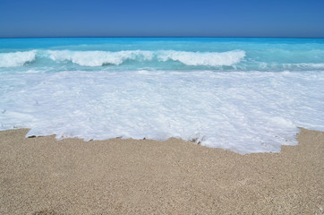 Sand, sea foam, turquoise waves and blue sky