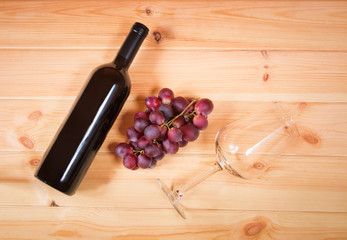 Bottle of red wine, purple grape and wine glass on wooden background