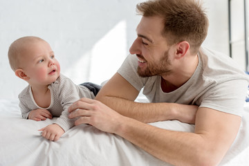 Fototapeta premium smiling father with little baby boy lying on bed