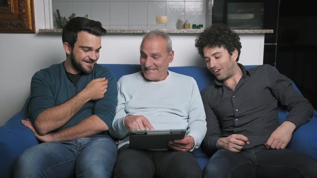 Father With his adult sons Looking At Digital Tablet on the couch,portrait