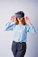 Red haired girl in blue blouse with vr glasses at studio isolated on white.