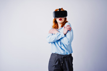 Red haired girl in blue blouse with vr glasses at studio isolated on white.