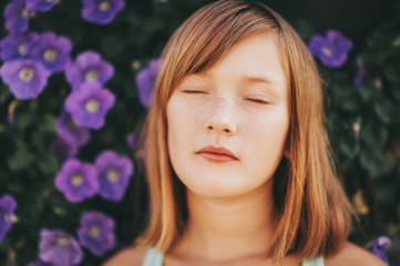 Fototapeta premium Daydreaming pretty kid girl, close up portrait against purple flower wall. Eyes closed